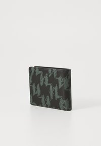 Portefeuille noir avec un motif géométrique vert, fabriqué en matériau texturé, présentant un design bi-fold compact avec des coutures visibles.