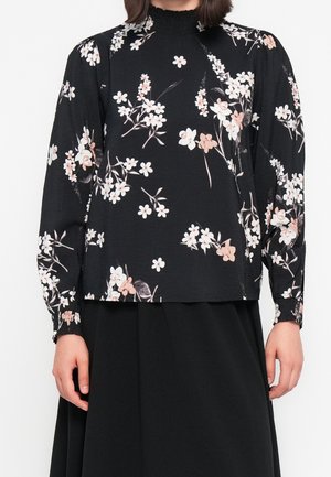 Sort langærmet bluse med høj hals og hvidt og lyserødt blomsterprint, kombineret med et sort skørt.