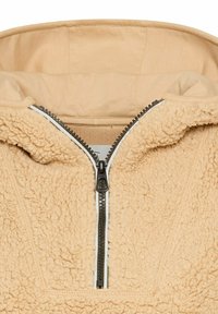 Beiger Fleece-Pullover mit einem Halb-Reißverschluss, strukturiertem Stoff und einem weichen Innenfutter. Mit kontrastierendem weißen Reißverschluss und Einfassung.