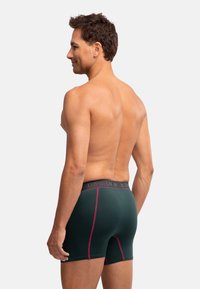 Pánské tmavě zelené boxerkové trenýrky mají hladký povrch, kontrastní růžové prošívání a elastický pas s logem.