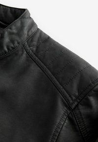 Detalle de chaqueta de cuero negra con un hombro acolchado, textura suave y un cuello alto. Acentos cosidos a lo largo de las costuras.