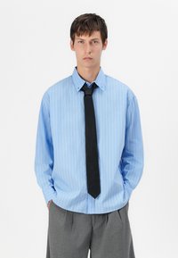 Camicia a righe blu chiaro con cravatta nera. La camicia presenta un colletto classico e maniche lunghe, con una vestibilità comoda e un orlo arrotondato.