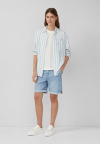 Light blue and white striped button-up shirt over a white t-shirt, paired with rolled-up light denim shorts and white sneakers.