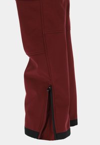 Vinrøde softshell-bukser med et elegant design. Har lodrette sidelommer med lynlåse ved benenden og en sort kant ved manchetterne for kontrast.