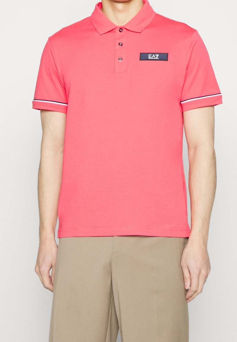 Polo corail en coton avec col à rabat, patte à trois boutons et accent bleu marine avec logo sur la poitrine. Manches courtes rayées.