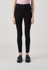 Svarta högmidjade byxor med en åtsittande design, tillverkade av elastiskt tyg. Har en knappstängning framtill och en halv längd vid vaden.