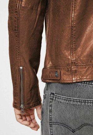Braune Lederjacke mit metallischem Glanz, ausgestattet mit Reißverschlussärmeln und einem Druckknopfverschluss an der Taille, kombiniert mit grauen Jeans.