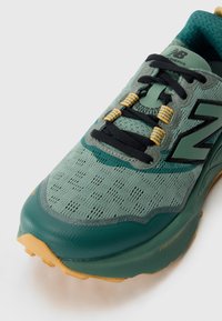 Light green running shoe with a mesh upper, black laces, and yellow accents. Features a textured sole for grip and a rounded toe design.
