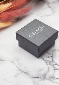 Svart texturerad smyckeslåda med ett slätt lock, prydd med vit upphöjd text som säger "Sofia Milani Jewels." Satt mot en marmorbakgrund.