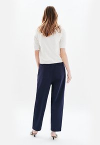 Vitt stickat kortärmat linne som matchas med marinblå löst sittande byxor. Skorna är låga klackar i metall. Enkla, rena linjer och minimal detalj.