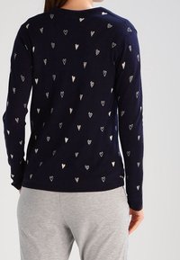 Maglione di lana navy con motivi a cuori bianchi sparsi, scollo rotondo e maniche lunghe, abbinato a pantaloni grigi. Morbido al tatto.