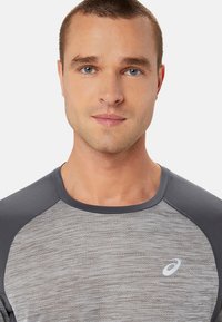 T-shirt sportivo da uomo in grigio con un motivo testurizzato, dotato di maniche raglan nere e un piccolo logo bianco sul petto.