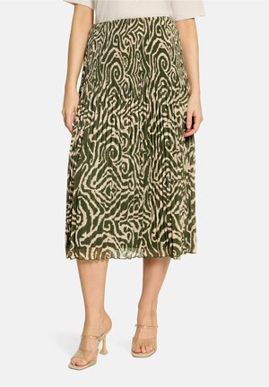 Woman wearing a midi pleated skirt with an abstract green and beige pattern and transparent high-heeled sandals against a white background.