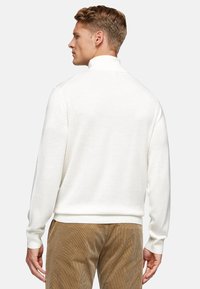 White pullover sweater with a high collar, made of textured fabric, featuring ribbed cuffs and hem. Worn with tan corduroy pants.