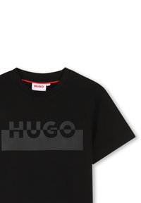 Zwarte katoenen T-shirt met korte mouwen, met een opvallend, textuurgegeven "HUGO" logo over de borst in een contrasterende matte afwerking.