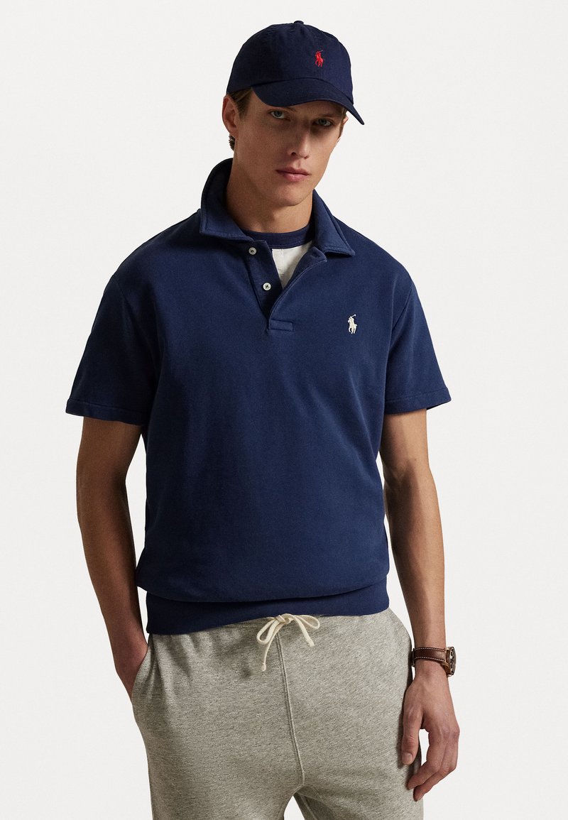 Navy blue cotton polo shirt with short sleeves, a collar, and three buttons; features a small white logo on the left chest. Gray pants.