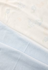 Couverture pour bébé en coton avec un dessus crème clair à motifs de chiens pastel et un fond doux et uni bleu clair. Texture lisse, forme rectangulaire.