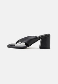 Black leather heeled sandal with wide crisscross straps and a block heel, shown from the side on a neutral background.