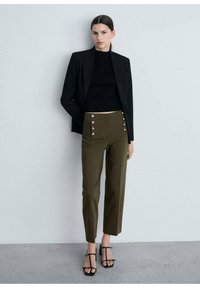 Mustap blazer mustan crop topin päällä, yhdistettynä oliivinvihreisiin korkeavyötäröisiin housuihin, joissa on sivunapit, sekä mustiin remmisandaaleihin.