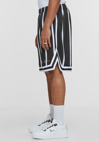 Svartvita randiga basketshorts med elastisk midja och sidoklipp, bärs tillsammans med vita sneakers och ankelsockor.