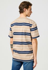Camiseta a rayas beige con rayas horizontales en azul marino y blanco, de manga corta y corte relajado. Material de algodón, cuello redondo.