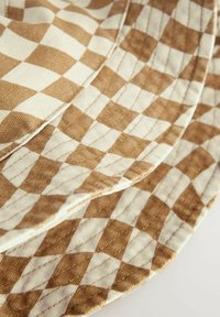 Tissu à carreaux marron et crème avec une finition texturée et des coutures visibles. Le motif présente des formes de diamants alternés.