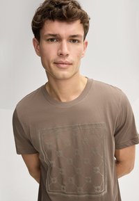 Bruine katoenen t-shirt met een subtiel geometrisch patroon in een lichte kleur. Korte mouwen en een ronde halslijn. Glad textuur.