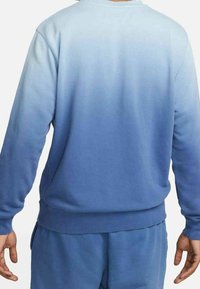 Světle modrý sweatshirt s modrým gradientem vyrobený z měkké tkaniny, přecházející z jasně modré na vrcholu do tmavě modré na spodní části. Má dlouhé rukávy a kulatý výstřih.