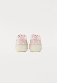 Baskets roses avec une finition lisse, dotées d'une semelle blanche épaisse et de la marque "HUGO" à l'arrière. Le design comprend des languettes de tirage et des cols rembourrés.