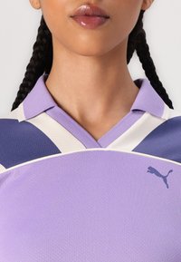 Camisa polo púrpura da Puma com design de gola, tecido texturizado e um detalhe com o logótipo na lateral. Blocos de cor branca e púrpura escura.