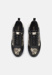 Un paio di sneakers nere stringate con motivi floreali dorati, suole bianche e linguette di estrazione, su sfondo bianco.