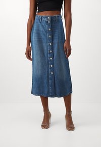 Denim midi kjol i ljusblått, med knapplist framtill, A-linjeform och fransdetalj i nederkanten. Bärs med genomskinliga klacksandaler.