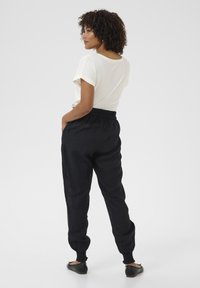 Pantaloni in lino leggeri e neri con vita elastica e caviglie risvoltate. Abbinati a una camicia color crema a maniche corte.