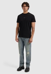 Zwart T-shirt met ronde hals en een klein gedrukt logo, gecombineerd met lichtblauwe versleten spijkerbroek en zwarte laarzen met dikke zool.