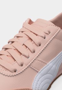 Κοντινό πλάνο απαλού ροζ αθλητικού παπουτσιού με υφασμένα κορδόνια και λευκή ραμμένη λεπτομέρεια στο πλάι πάνω σε λείο δερμάτινο μέρος.