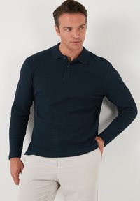 Polo de manga larga en azul marino, hecho de tela acanalada, con una tapeta con botones y un cuello clásico. Textura suave, diseño ajustado.