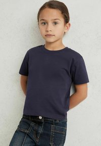 Tumši zils īsām piedurknēm T-krekls ar apaļu kaklu, apvienots ar tumšu džinsu biksēm, kurām ir priekšējās un aizmugurējās kabatas. Gluda kokvilnas auduma.