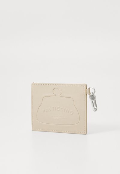 Beige ādas maks ar iegravētu dizainu un sudraba furnitūru, ar aizdari un noapaļotu formu, kura izmērs ir aptuveni 10 x 10 cm.