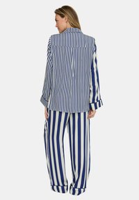 Gestreifter Pyjama-Set in Marineblau und Weiß, bestehend aus einem langärmligen Hemd mit Kragen und passenden locker sitzenden Hosen mit aufgekrempelten Bündchen.