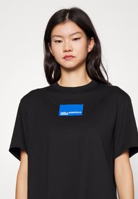 Camiseta de algodón negra con cuello redondo y mangas cortas, que presenta un estampado de logo rectangular azul que dice "KARL LAGERFELD JEANS."
