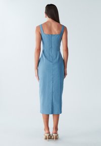 Zila, pieguloša midi kleita ar kvadrātveida izgriezumu, bez piedurknēm un aizmugurēju rāvējslēdzēju. Gluda, viegla auduma ar taisnu apakšmalu.