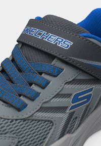 Παντόφλα Skechers σε γκρι και μπλε χρώμα με ύφασμα από δίχτυ, ριγωτά κορδόνια και λουρί Velcro που φέρει το λογότυπο Skechers.