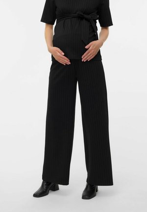Schwarzes, gestreiftes Umstandstop mit gebundenem Bund, kombiniert mit weiten, gestreiften schwarzen Hosen und schwarzen Stiefeletten mit Absatz.