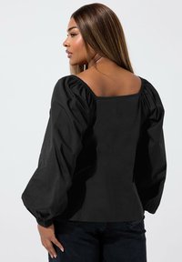 Svart puffärmad topp med fyrkantig utskärning och texturerad tyg. Har en passform och utställd design samt elastiska manschetter på ärmarna.