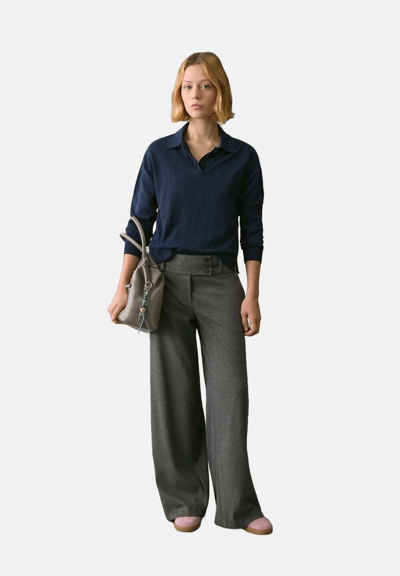 Suéter de punto azul marino con un diseño de cuello, combinado con pantalones de pierna ancha gris. Un bolso beige y zapatos rosa claro completan el look.
