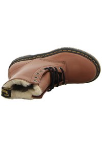 Botas de tobillo de cuero marrón con un suave forro de piel, cordones negros y ojetes metálicos. Presentan una suela cosida en negro y amarillo.