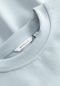Φωτεινό γαλάζιο βαμβακερό t-shirt με στρογγυλή λαιμόκοψη και ορατή λευκή ετικέτα που γράφει "NOELLA" στο εσωτερικό του γιακά.