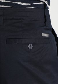 Marinblå tygshorts med en bakficka som har en knappstängning. Inkluderar en silverfärgad metalltagg präglad med "Armani Exchange."