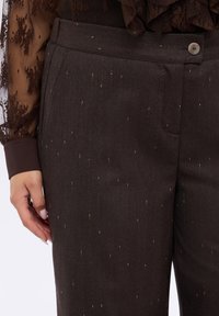 Brązowe spodnie z subtelnym wzorem w delikatne prążki i metalicznymi złotymi drobinkami. Charakteryzują się gładką fakturą i zapięciem na guzik.