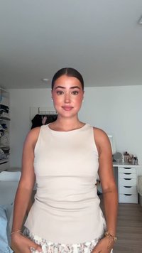 Bež brezrokavnik s prilegajočim telesom in širšo spodnjo robom, v kombinaciji z vzorčasto krilom. Enostaven dizajn, gladka tekstura, subtilni detajli.